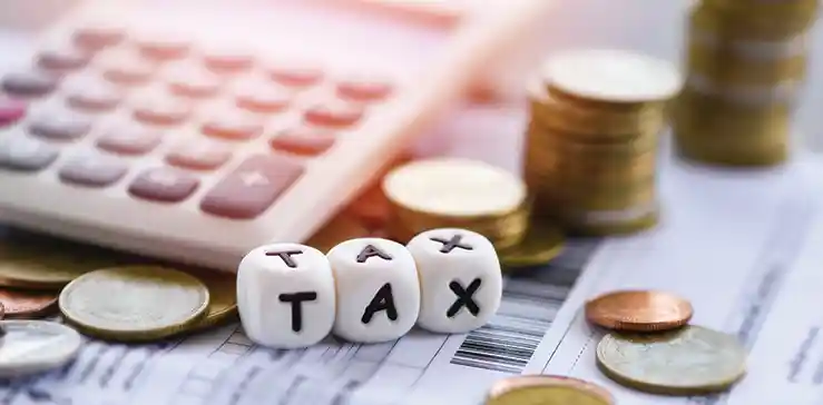 A calculator, coins, and dice spelling "TAX" on financial documents illustrate tax preparation and financial planning.
